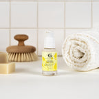 Skincare bottle with a yellow label on a bathroom counter with a towel and brush in the background.