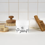 "get-Glamrus" jar of Icelandic Volcano Face & Body Scrub on a bathroom counter with a scrubber, soap, and comb in the background.